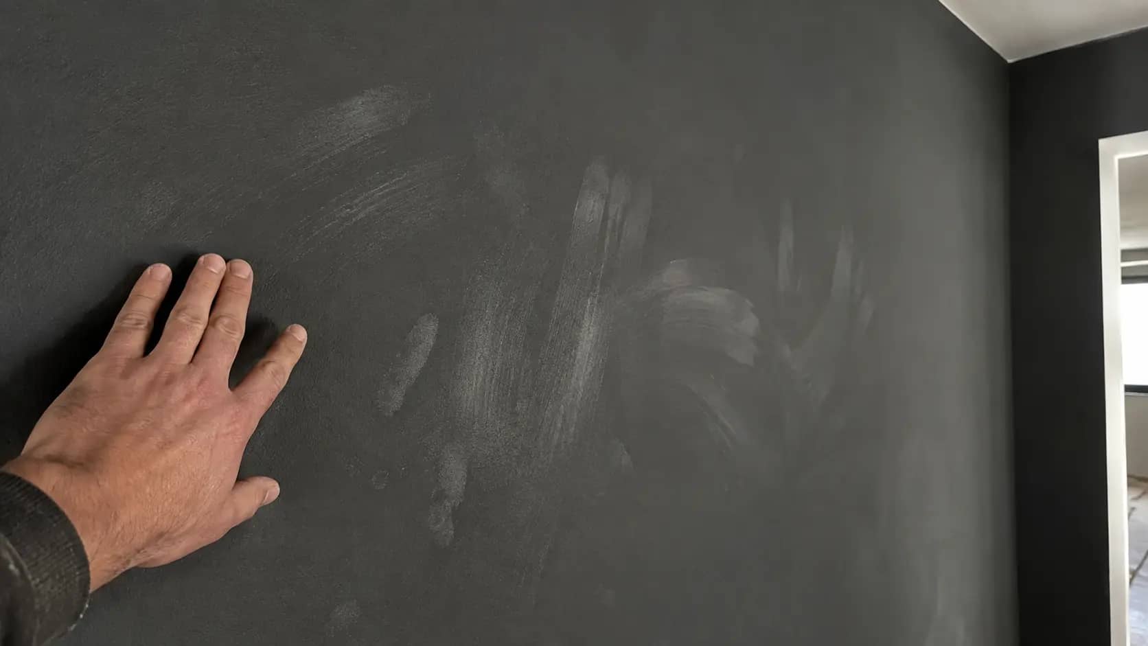 Hand an einer dunklen matten Wand mit hellen Streifen durch den Schreibeffekt, Malerbetrieb Rekowski Magdeburg